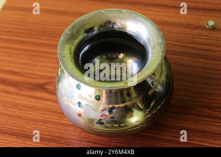 Vaso in acciaio in ottone "Kalash" (lota), un tradizionale contenitore d'acqua globulare, posto su uno sfondo marrone legno, che mette in risalto la sua cultura e utilità Foto Stock