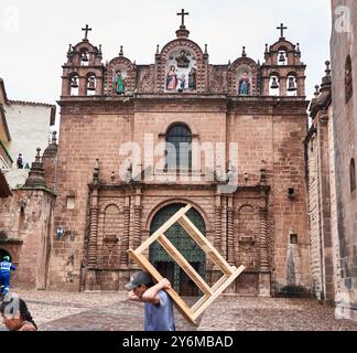 Vista della facciata storica della chiesa di Cusco, in Perù, con persone che camminano di fronte. Cattura la bellezza architettonica e la vita quotidiana in un ambiente culturale. Foto Stock