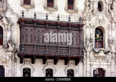 Primo piano di una dettagliata facciata coloniale con un balcone in legno ornato e decorazioni festose a Lima, Perù. Cattura l'eleganza e la storia Foto Stock