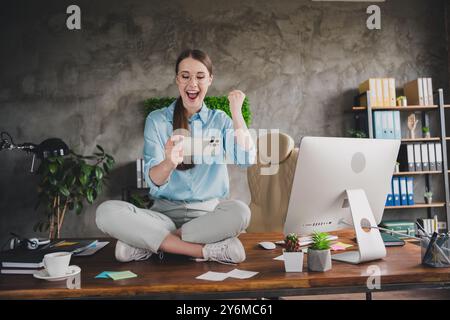 Foto del fortunato broker donna positivo indossare camicia occhiali da vista tavolo da seduta gioco vincente gadget moderno al chiuso officina sul posto di lavoro Foto Stock