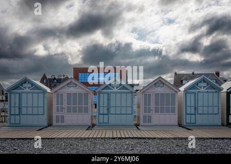 Cayeux-sur-Mer, Francia - 09 17 2024: Veduta delle colorate cabine dipinte sulla spiaggia con sentieri in legno, ciottoli e un cielo nuvoloso Foto Stock