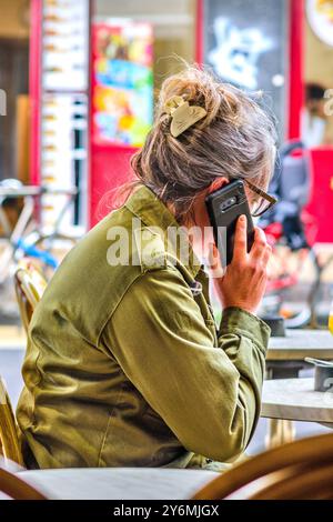 Una donna sedeva al tavolo del caffè parlando al telefono cellulare - Tours, Indre-et-Loire (37), Francia. Foto Stock
