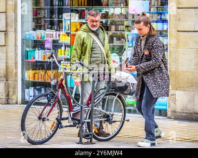 Una giovane donna che chiude la sua bici Decathlon City Bike nel centro della città con uno spettatore che guarda - Tours, Indre-et-Loire (37), Francia. Foto Stock