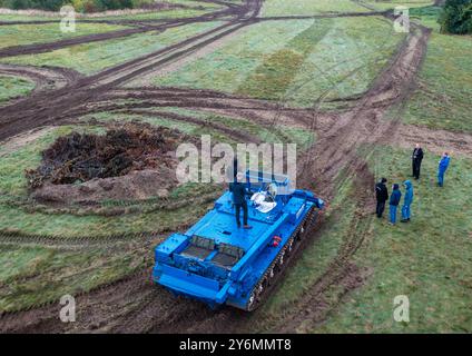 26 settembre 2024, Meclemburgo-Pomerania occidentale, Schwerin: Un veicolo blindato T55 di produzione russa è utilizzato da un'azienda privata per le operazioni di incendi boschivi e disastri per preparare un'area di compensazione della natura alla periferia della città per l'insediamento di rettili. (Vista aerea con un drone) al fine di garantire una migliore protezione delle specie, il prato deve essere dotato di una nuova struttura del suolo con l'uso di attrezzature pesanti. La città deve regolarmente trasferire lucertole di sabbia, rospi di tonnetto e altre specie protette quando le aree precedentemente inutilizzate sono preparate per la struttura Foto Stock