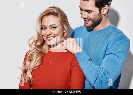 Regalo di lusso. Bel giovane uomo che indossa una nuova collana sulla sua ragazza e sorride mentre sta in piedi su sfondo grigio Foto Stock