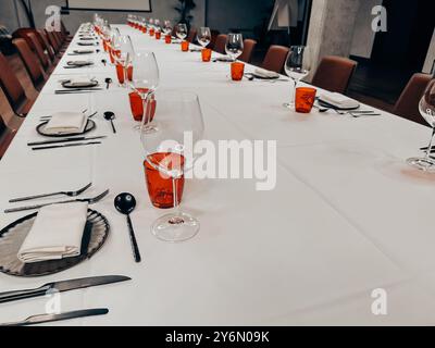 Tavolo in un ristorante. Vetreria, bicchieri rossi su una tovaglia bianca su un tavolo. Utensili per mangiare e bere. Forche e coltelli piastre con tovaglioli Foto Stock