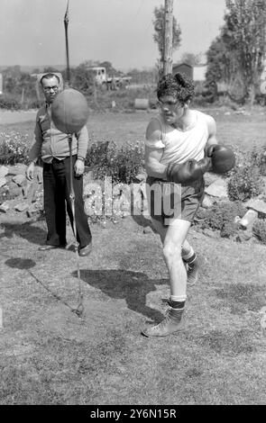 Tousled Freddie Mills, campione mondiale dei pesi mediomassimi, si aggira al pugno all'aria aperta al campo da badley, Betchworth, Surry, dove i mulini si trovano ora nella fase finale di allenamento per la sua lotta con Bruce Woodcock al White City Stadium di Londra, il 2 giugno.a guardare c'è l'allenatore di Nat Sellars Mills. 18 maggio 1949 Foto Stock