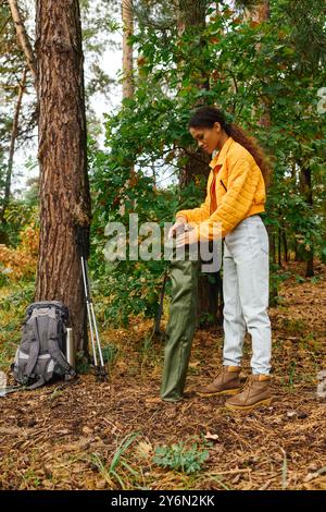 Esplorando la vibrante foresta autunnale, una giovane donna si prepara per un'escursione avventurosa, che si collega con la natura. Foto Stock