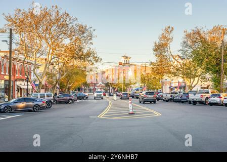 Sag Harbor, New York - 23 ottobre 2023: Vista della strada principale fiancheggiata da edifici storici in mattoni e alberi al tramonto. Foto Stock