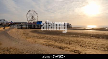 Un tranquillo tramonto su una spiaggia sabbiosa con un molo e una ruota panoramica. Foto Stock