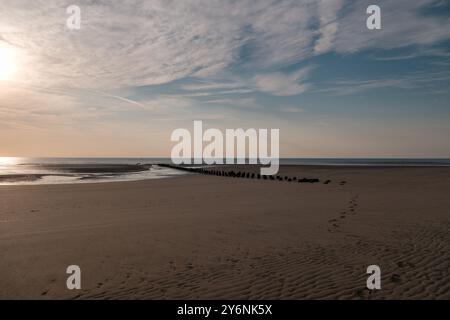 Spiaggia tranquilla con sabbia ondulata e un molo lontano sotto un cielo pastello al tramonto. Foto Stock