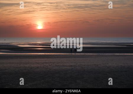 Due persone ammirano un tranquillo tramonto sulla vasta e riflettente costa. Foto Stock