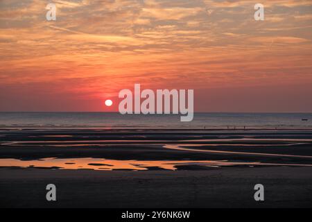 Tramonto tranquillo su una spiaggia con bassa marea, con piscine d'acqua riflettenti e un cielo in pendenza. Foto Stock