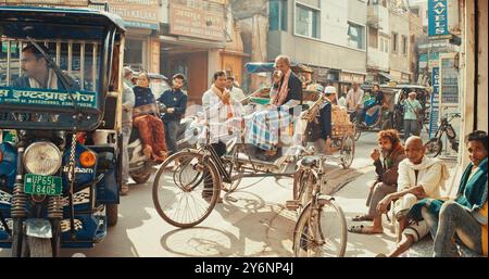 Varanasi, India. La gente cammina lungo la strada trafficata. I conducenti di Mans Rickshaw riposano e bevono caffè. Traffico su Street Motion. Motociclette, in movimento per strada Foto Stock