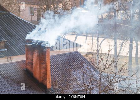 Dal camino in mattoni sul tetto della casa proviene del fumo intenso. Il tema della crisi del gas. Il concetto di riscaldamento globale e po ambientale Foto Stock