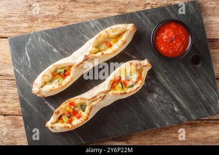 Pizza sorrentina vegetariana con mozzarella e provolone e peperoni, pomodori, carciofi, zucchine primo piano su un tavolo in ardesia sul tavolo. Ho Foto Stock