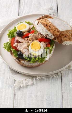 Panino francese Pan Bagnat con insalata nicoise in speciale pane di segale primo piano su un tavolo di legno. Verticale Foto Stock