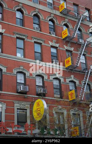 New York, Stati Uniti - 26 settembre 2024: Facciata di un edificio urbano a Chinatown con fughe antincendio e cartelli gialli cinesi. L'immagine mostra t Foto Stock