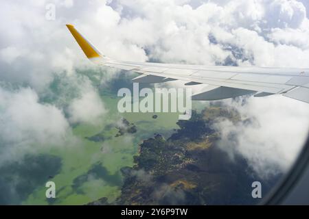 Ala di un aereo passeggeri che sorvola il lago di Skadar in Montenegro. Vista mozzafiato dalla finestra dell'aereo di nuvole, lago verde, isole e costa Foto Stock