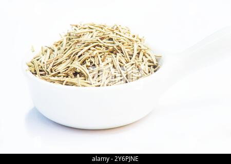 Foglie di rosmarino essiccato (rosmarinus officinalis) in una ciotola bianca su sfondo bianco Foto Stock