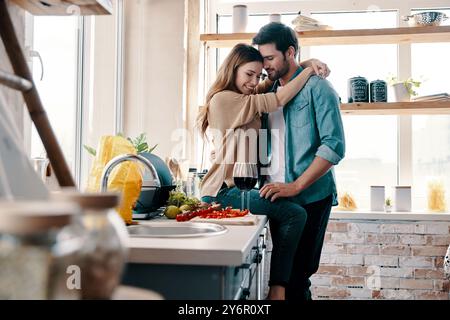 Allontanarsi da tutto... Bella coppia giovane che prepara la cena e beve vino mentre si trova in cucina a casa Foto Stock