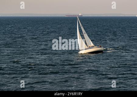 Yacht a vela di fronte a una nave cargo all'orizzonte. Borstahusen, Landskrona kommun, Skåne, Svezia Foto Stock