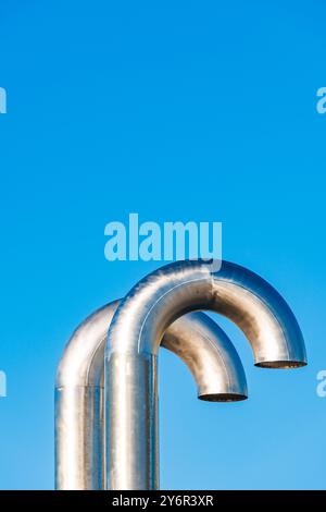 Due tubi in metallo ricurvi si distinguono contro un cielo blu vibrante e presentano un design industriale. La scena riflette un'estetica ingegneristica moderna Foto Stock