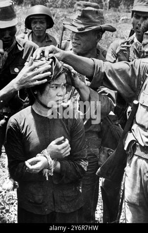 10 MAGGIO 1962 I SOLDATI DEL VIETNAM DEL SUD PREDANO UNA RAGAZZA ACCUSATA DI SPIONAGGIO PER I GUERRIGLIERI COMUNISTI DEL NORD METTENDO UNA CAP ROSSA SULLA SUA TESTA. TRUONG HOA, VIETNAM. Foto Stock