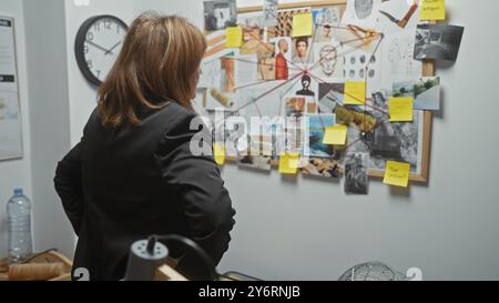 La donna indaga sulle prove del crimine sulla bacheca di sughero nell'ufficio investigativo, analizzando indizi al chiuso. Foto Stock