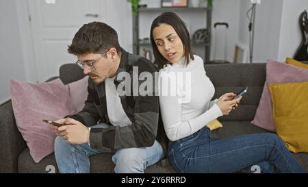 Una donna guarda segretamente il telefono di un uomo mentre si siedono insieme su un divano in un salotto moderno. Foto Stock