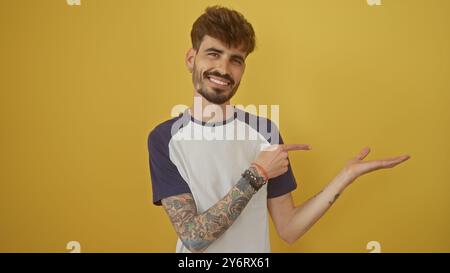 Bell'uomo sorridente con barba e tatuaggi che puntano felicemente su sfondo giallo Foto Stock