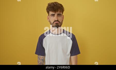 Un giovane ispanico con la barba si posa su un isolato sfondo giallo, sembra bello e serio. Foto Stock