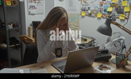 La giovane detective stressata alla sua scrivania circondata da prove di casi in un ufficio della stazione di polizia. Foto Stock