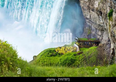 I turisti con gli impermeabili gialli visitano le spettacolari cascate Niagara Horseshoe sul fondo della cascata durante l'escursione Journey Behind the Falls Foto Stock