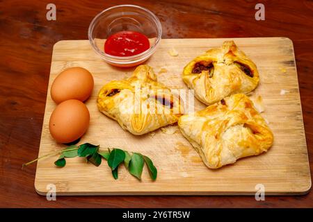 Primo piano immagine dei gustosi braccialetti d'uovo in stile Kerala con salsa di pomodoro, foglie di curry e uovo su tagliere. Sfondo in legno Foto Stock