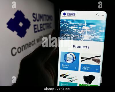 In questa illustrazione fotografica, una persona ha in mano un cellulare con la pagina Web dell'azienda giapponese Sumitomo Electric Industries Ltd. Davanti al logo. Foto Stock