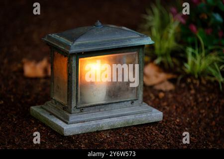 primo piano di una vecchia lanterna funeraria con una candela in fiamme su una tomba al crepuscolo Foto Stock