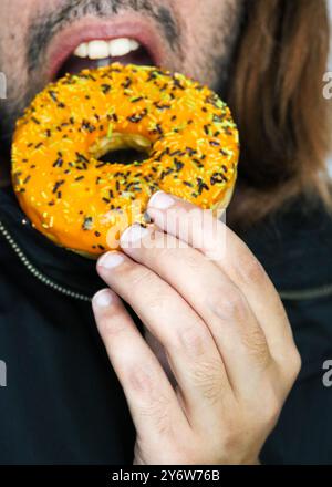Un tizio che mangia una ciambella a tema halloween, sta per morderla, bocca aperta Foto Stock