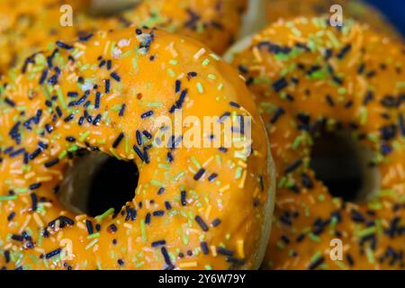 Ciambelle a tema Halloween con glassa arancione, primo piano con spruzzette di bianco e nero Foto Stock