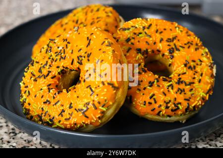 Ciambelle a tema Halloween con glassa arancione, spruzzette di bianco e nero Foto Stock