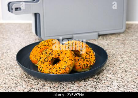 Ciambelle a tema Halloween con glassa d'arancia, spruzzi di bianco e nero su un piatto in cucina Foto Stock