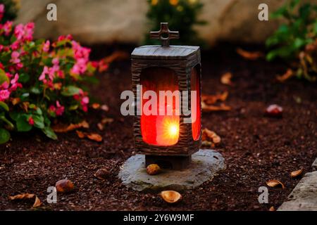 lanterna con candela ardente al crepuscolo su una tomba autunnale con alcune foglie autunnali cadute e castagne Foto Stock