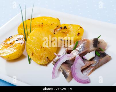 Fette di aringa mite-curata con patate fritte e cipolle servite sul piatto Foto Stock