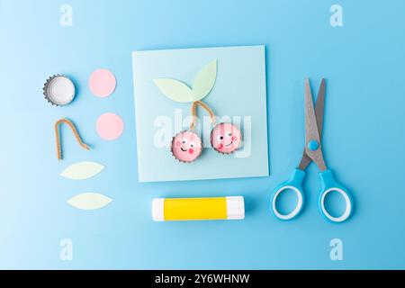 Modello di carta a tema ciliegia in blu con forbici su carta, parte di un progetto artigianale per bambini. Perfetto per attività fai-da-te e apprendimento creativo Foto Stock