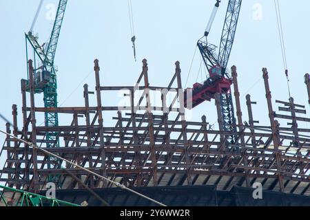 Una giornata lavorativa nel cantiere. Lavoratori in altezza, travi in acciaio, gru e cavi. Foto scattata in una giornata di sole. Foto Stock