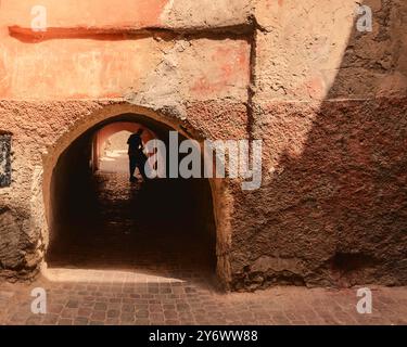 La silhouette di una persona che cammina in bicicletta attraverso un passaggio ad arco in una strada strutturata e intemprata nell'antica Marrakech, nella Medina, in Marocco, Foto Stock