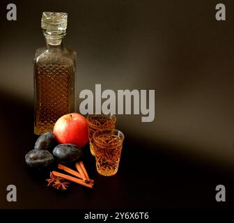 Liquore prugna-mela con spezie su sfondo nero, alcol forte in un vetro di cristallo con cannella e anice. Primo piano. Foto Stock