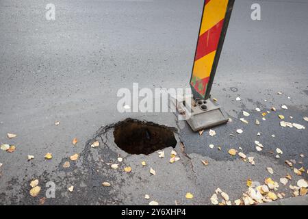 Dettagli con una grande buca nel mezzo di una strada asfaltata con le auto che passano Foto Stock