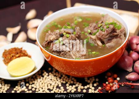 Zuppa di costolette di coda di bue o zuppa di manzo in una ciotola rossa con ingredienti su sfondo in legno, fotografia ravvicinata per il ristorante con menu banner, poster per volantini Foto Stock