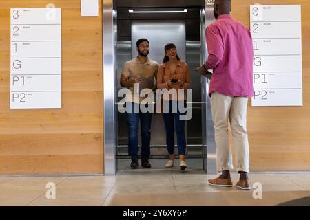 Uscendo dall'ascensore, uomo e donna sorridenti e salutano il collega nell'edificio degli uffici Foto Stock